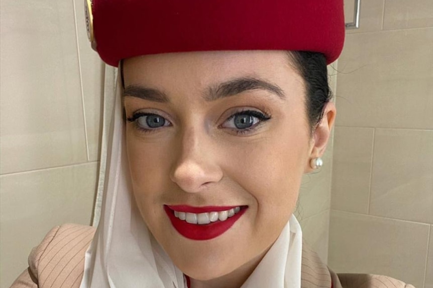 A Caucasian woman wearing red lipstick, winged eyeliner and a red round hat smiles in a selfie