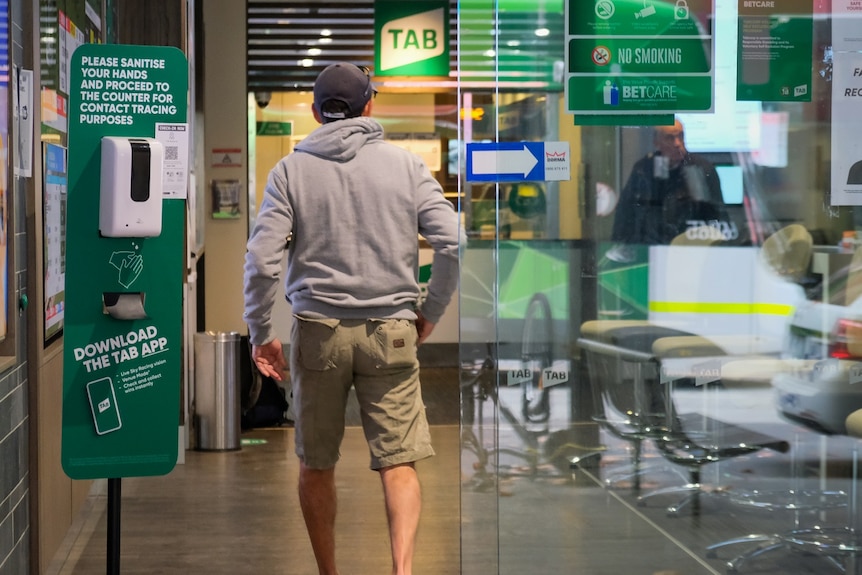 Un hombre entra por la puerta corrediza de vidrio del Melbourne TAB.