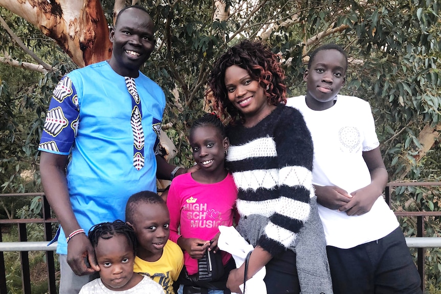 Philip Lako stands in front of Australian trees with his wife and four children. 