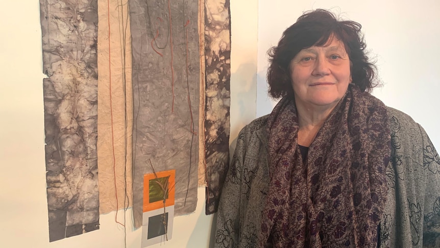 Donna Caffrey stands in front of a fabric and paper hanging textile in a gallery space