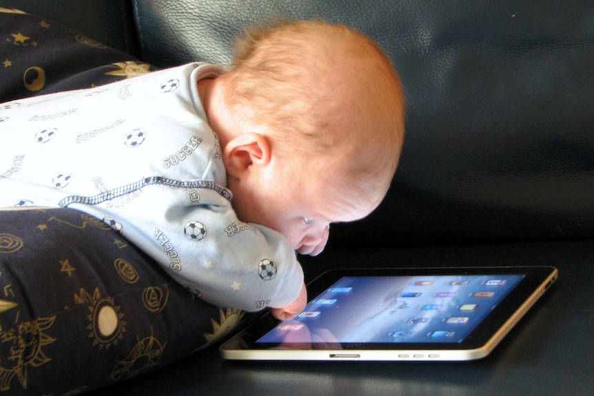 A baby with an iPad on a couch