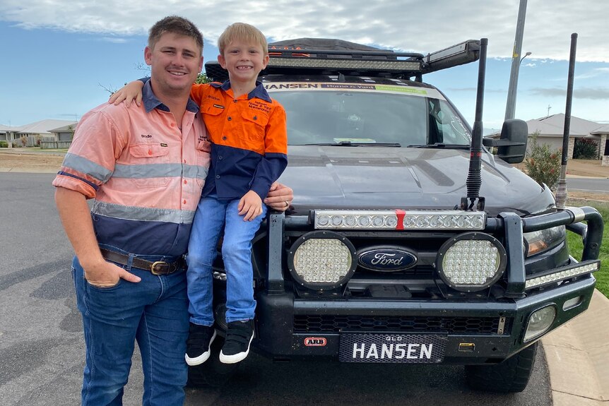 Smiling man holding his young son in front of large ute.