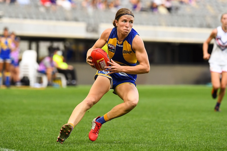 An AFLW player pivots off her right foot to head in-field with the ball as she runs in space during a game..