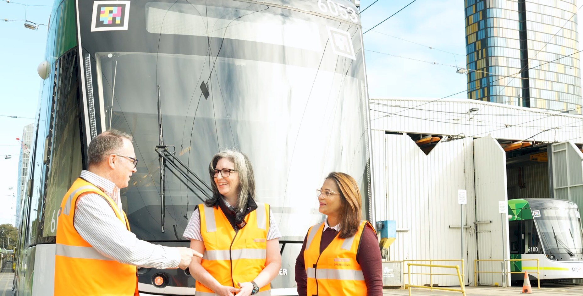 Two women standing beside a man in front of a tram talking to each other