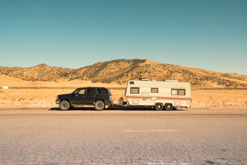 A black SUV car is connected to a white caravan with a desert scene in the background