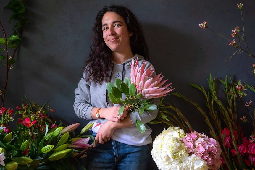 A woman standing surrounded by colourful bunches of flowers.