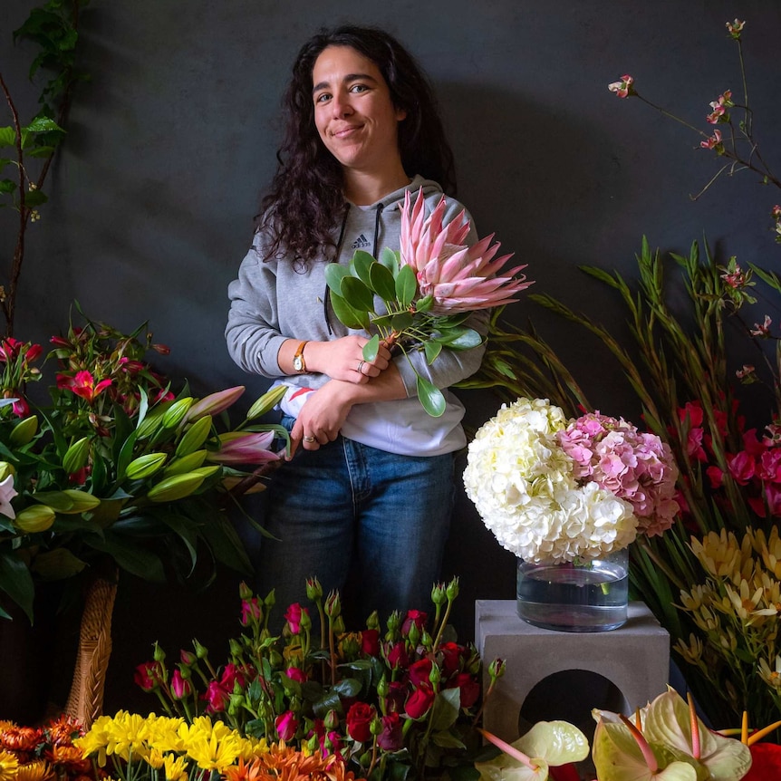 A woman standing surrounded by colourful bunches of flowers.