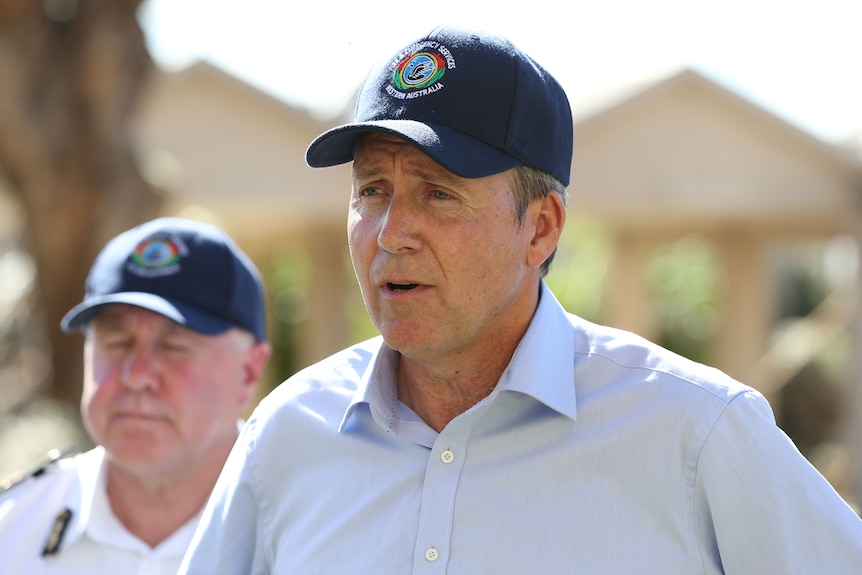 A man in a blue shirt and a blue cap stands at a press conference