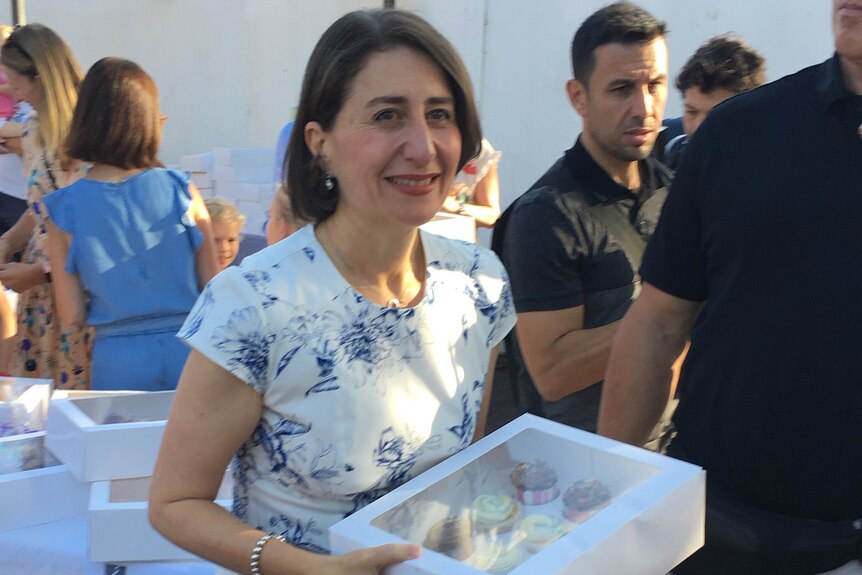 Premier Gladys Berejiklian buying cupcakes from a stall after voting on Saturday morning