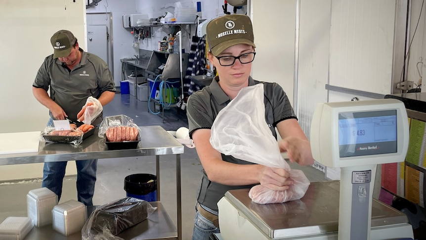 Woman in foreground and man in background both working in a butcher shop