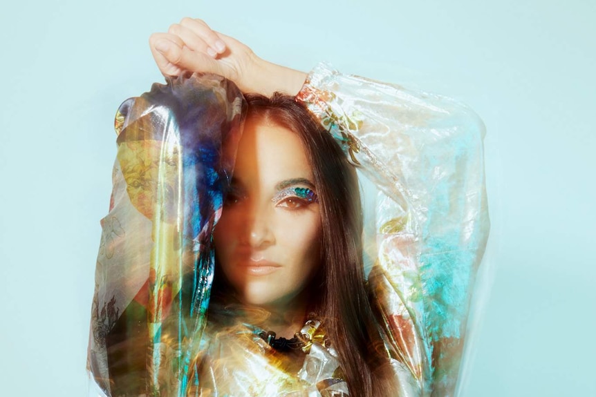 A photograph of Angel Dixon wearing a colourful dress posing in front of a pale blue background.