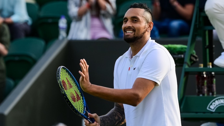 A smiling Nick Kyrgios claps his racquet to applaud the crowd after a win at Wimbledon.