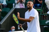 A smiling Nick Kyrgios claps his racquet to applaud the crowd after a win at Wimbledon.