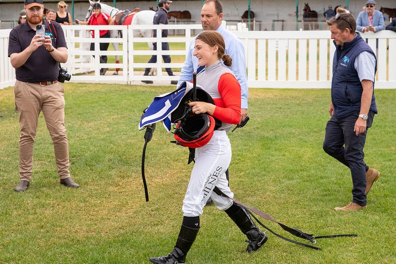 Rochelle smiles in her jockey silks and helmet to a crowd of supporters.