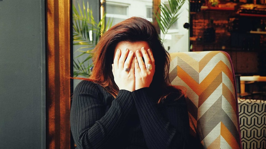 Woman with dark hair cradling her head in her hands