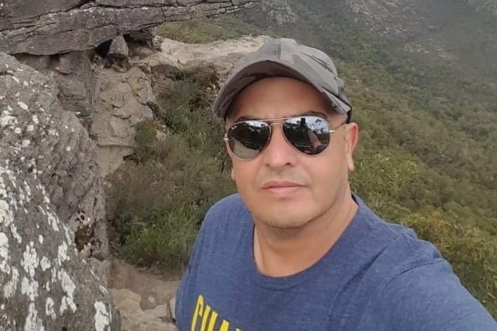A man wearing a blue t-shirt and sunglasses takes a selfie, possibly in Victoria's Grampians.