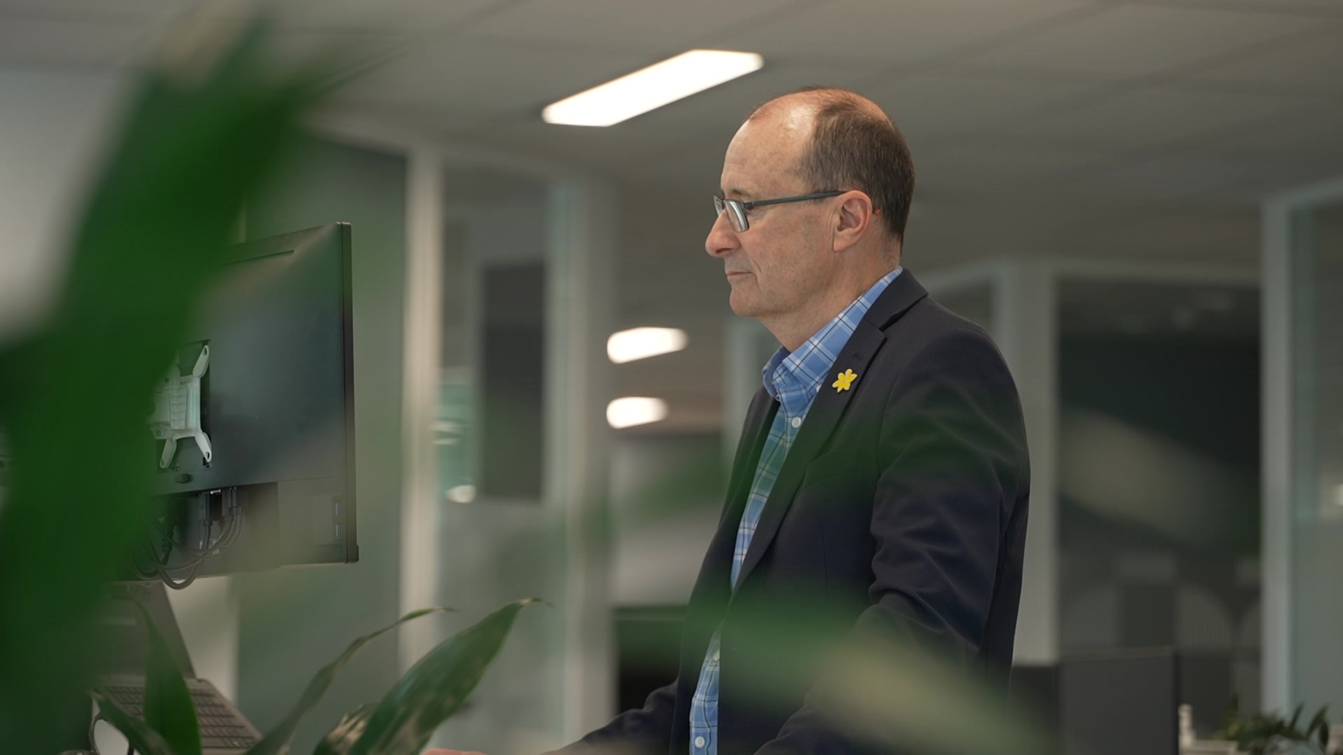Craig Sinclair working looking at his computer, part of plant blurred to the left