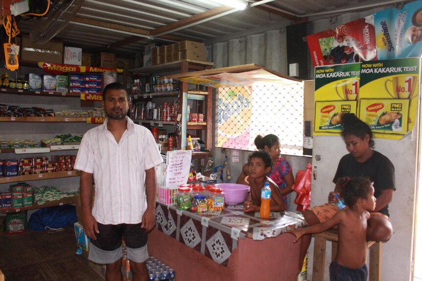 Un homme sud-asiatique vêtu d'une chemise légère se tient devant une femme et deux enfants dans un magasin général