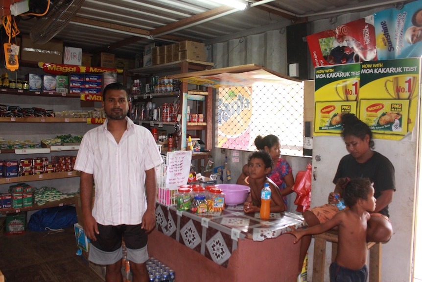 A South Asian man in a light shirt stands in front of a woman and two children in a general store