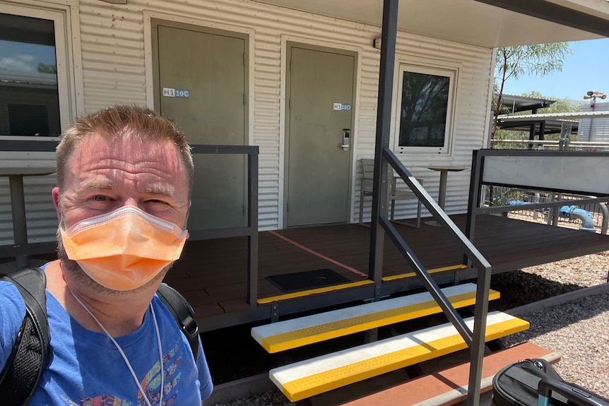 A man in a mask standing on a street bathed in sunlight.