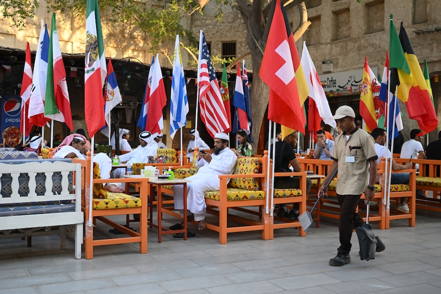 A number of people sit at tables in an outdoor bar, surrounded by flags of World Cup nations