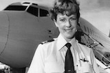 Black and white photo of smiling woman in pilot uniform standing in front of grounded Ansett aeroplane.