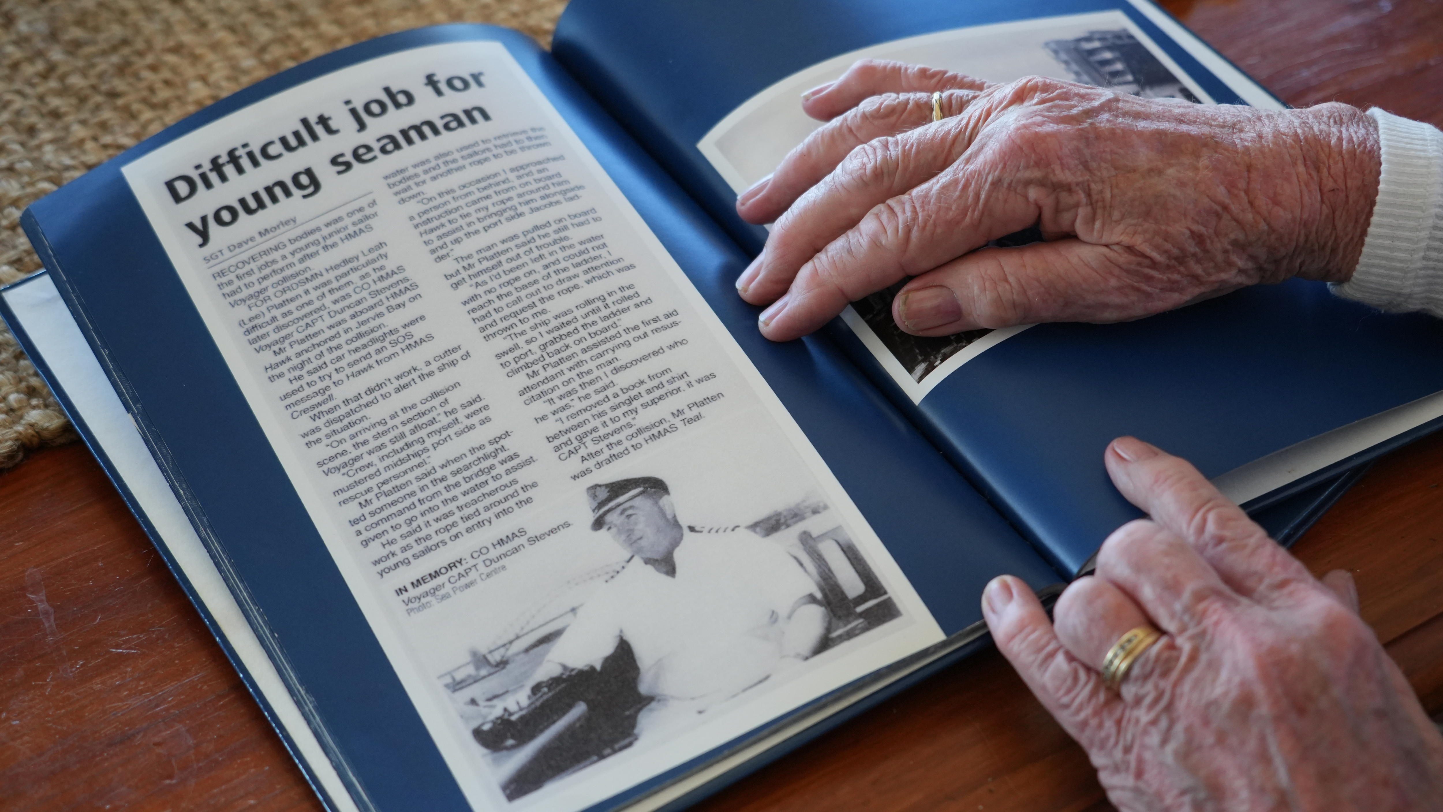 A newspaper clipping glued to a book, with hands holding the pages open. The headline reads: "Difficult job for young seaman".