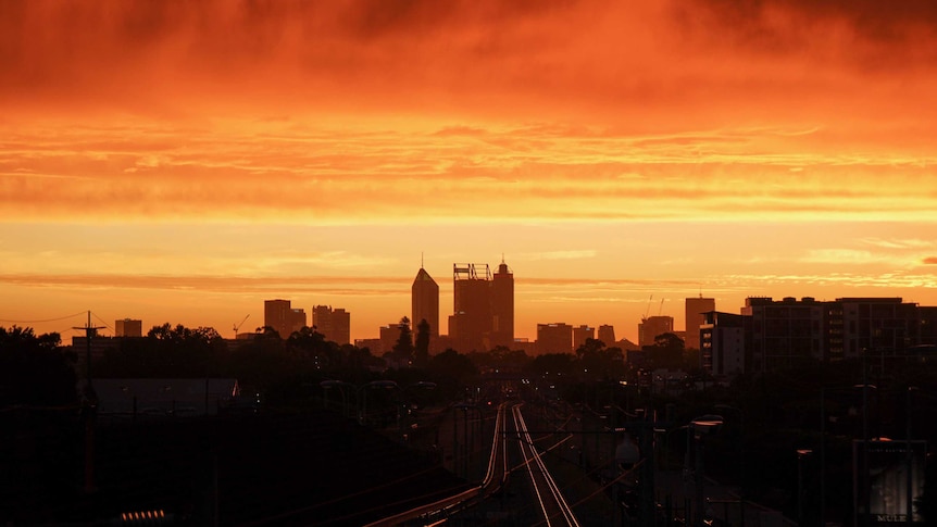 A long shot of Perth's CBD at sunset, with a bright orange and yellow sky enveloping the city skyline.