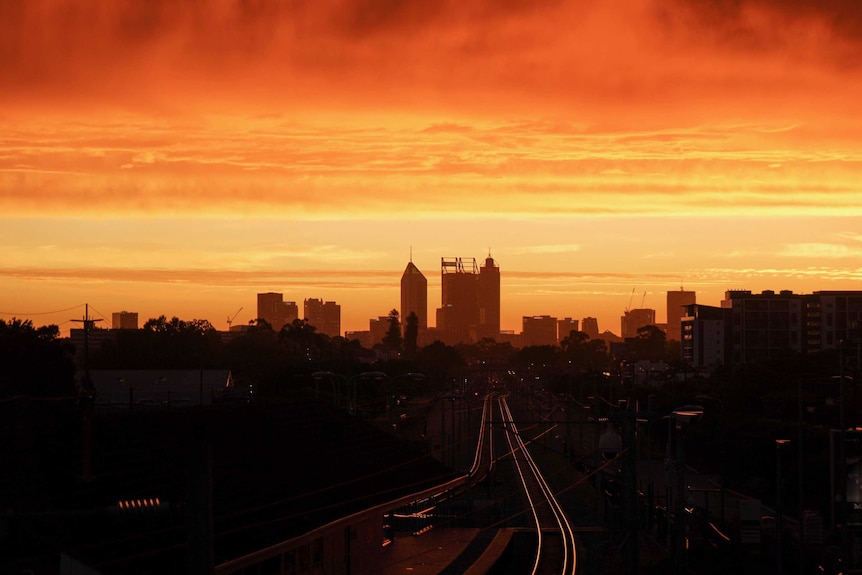 A long shot of Perth's CBD at sunset, with a bright orange and yellow sky enveloping the city skyline.