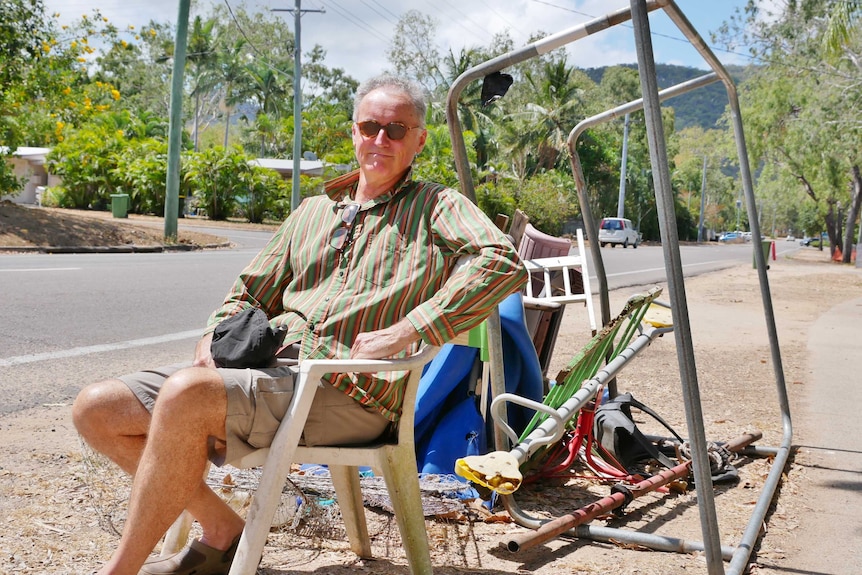 man in striped top sitting in old chair in front of a pile of rubbish