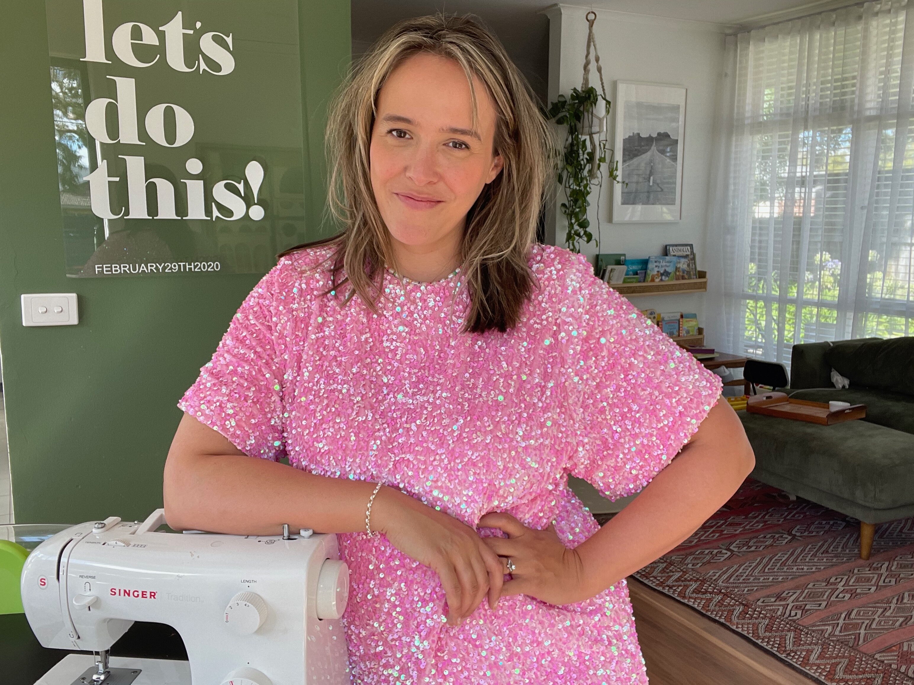 Bec Brewin beside a sewing machine in a pink sequinned dress she's been altering for the Taylor Swift Eras tour in Australia