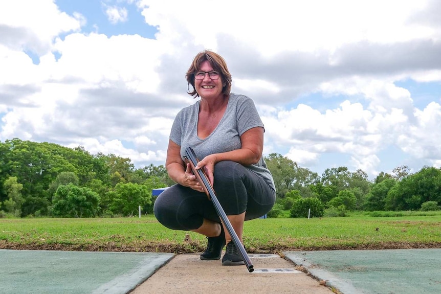 Deserie Baynes crouches down in front of the shooting range and while holding her gun.