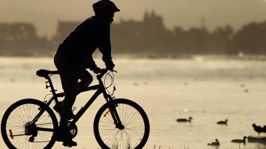 A cyclist rides next to a lake.