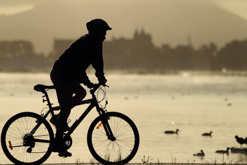 A cyclist rides next to a lake.