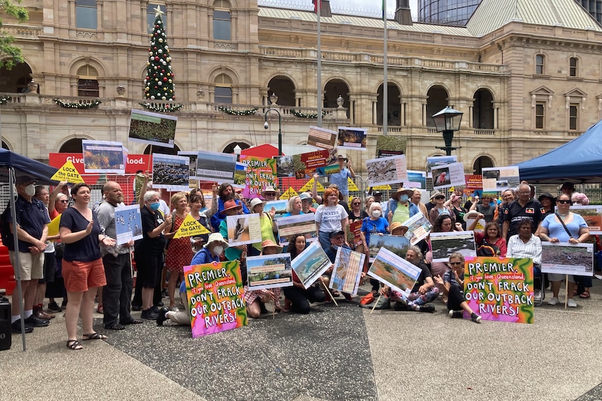 A large group of protesters stand together with signs condemning gas exploration in the Lake Eyre Basin