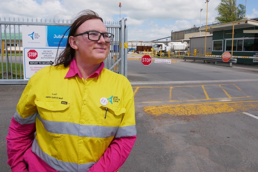 A woman smiles and stares into the distance outside a timber mill