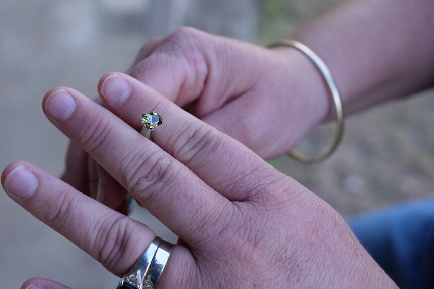 A close up of a hand holding a cut green sapphire