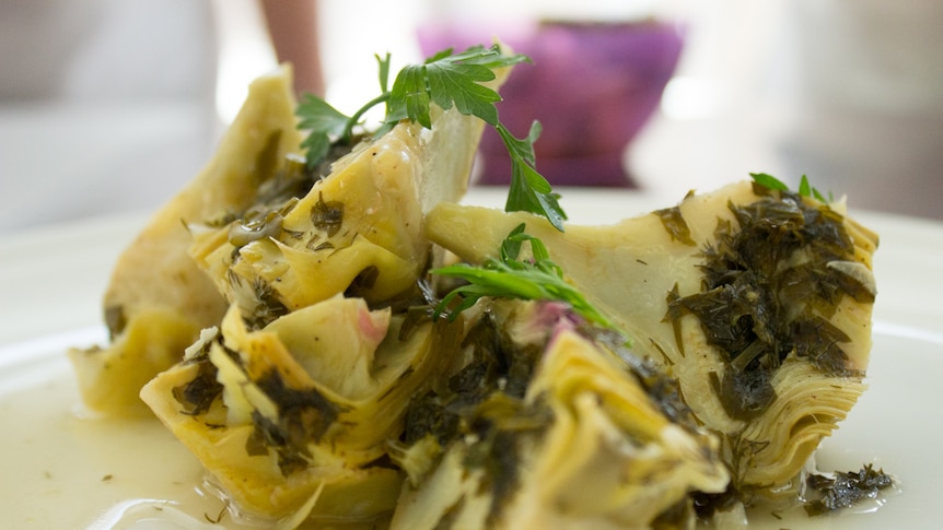 A small pile of cooked herbed artichokes on a white plate.