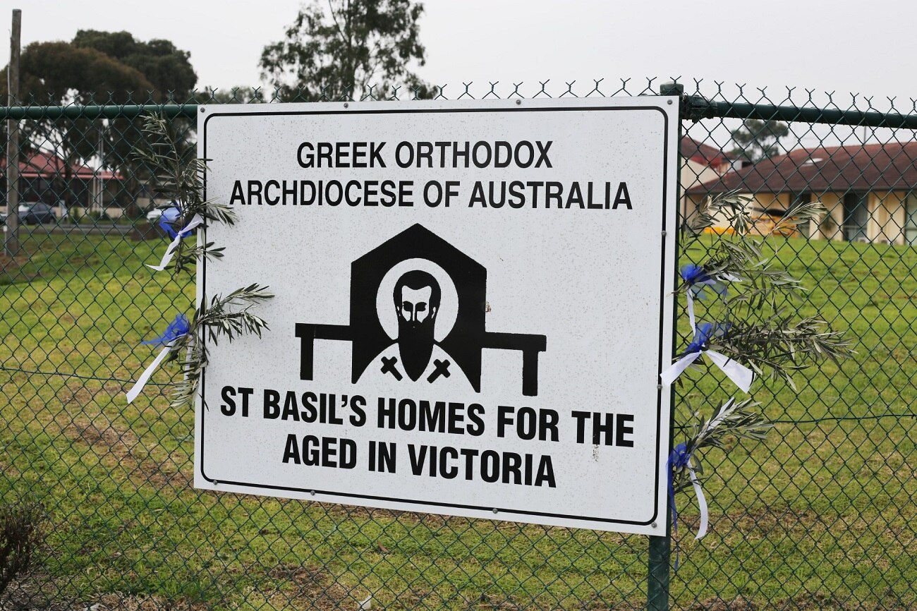 A sign on the fence outside St Basil's Homes for the Aged has olive branches and blue and white ribbons tied to its sides.
