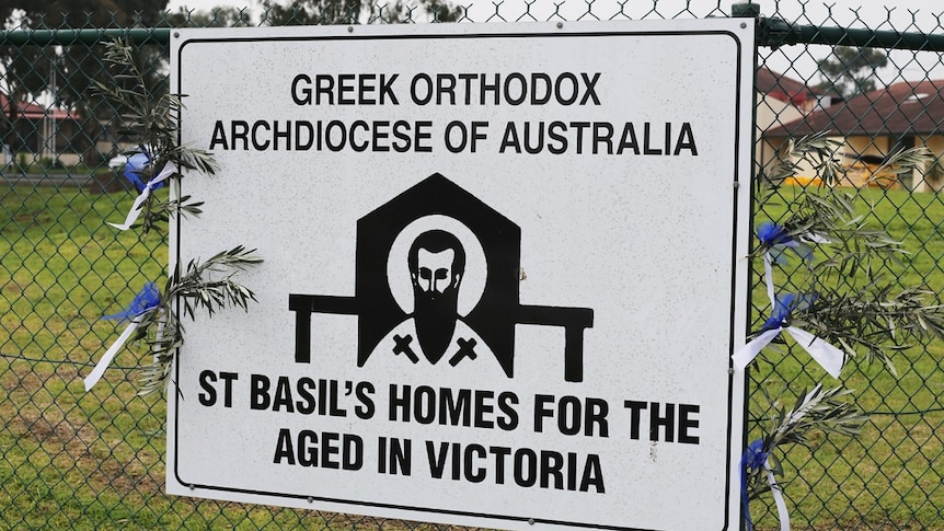 A sign on the fence outside St Basil's Homes for the Aged has olive branches and blue and white ribbons tied to its sides.