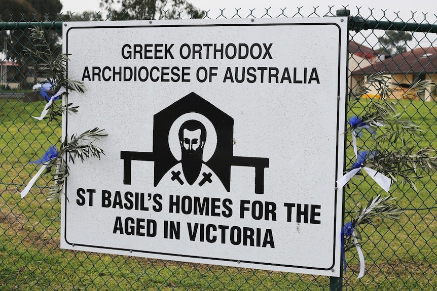 A sign on the fence outside St Basil's Homes for the Aged has olive branches and blue and white ribbons tied to its sides.