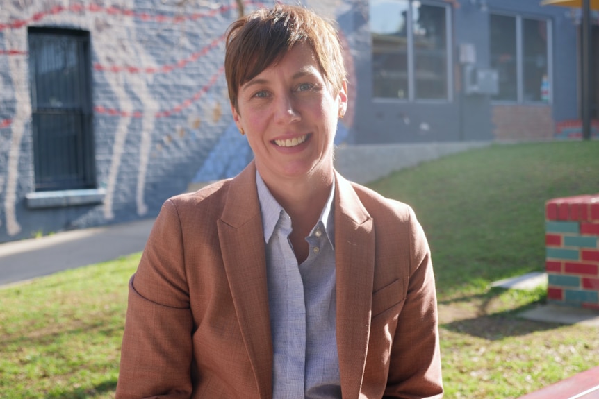 A woman in a brown jacket stands in a park