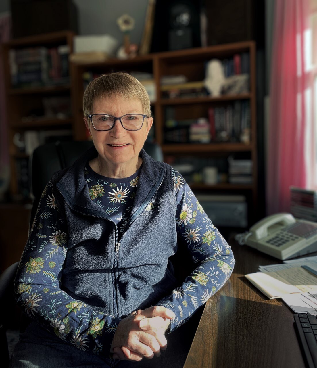 Mary smiles sitting at her desk.