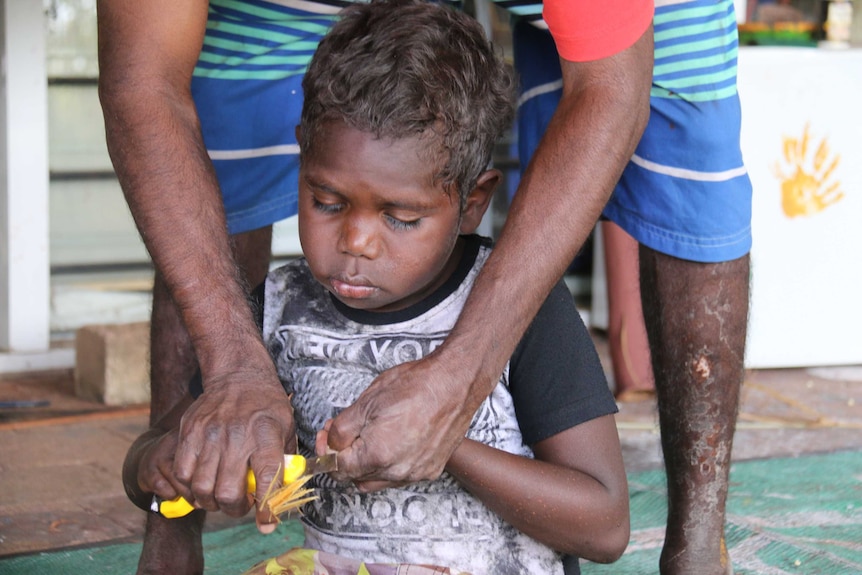 A child learning how to make a paintbrush from grass at the Children's Ground centre in Jabiru.