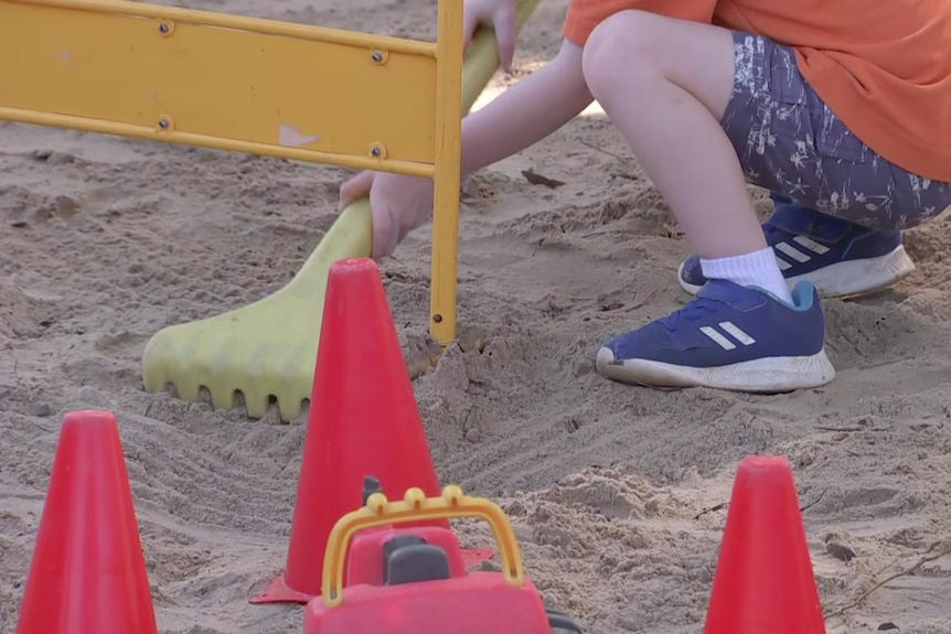 A child playing in the sand with a rake, surrounded by cones and trucks.