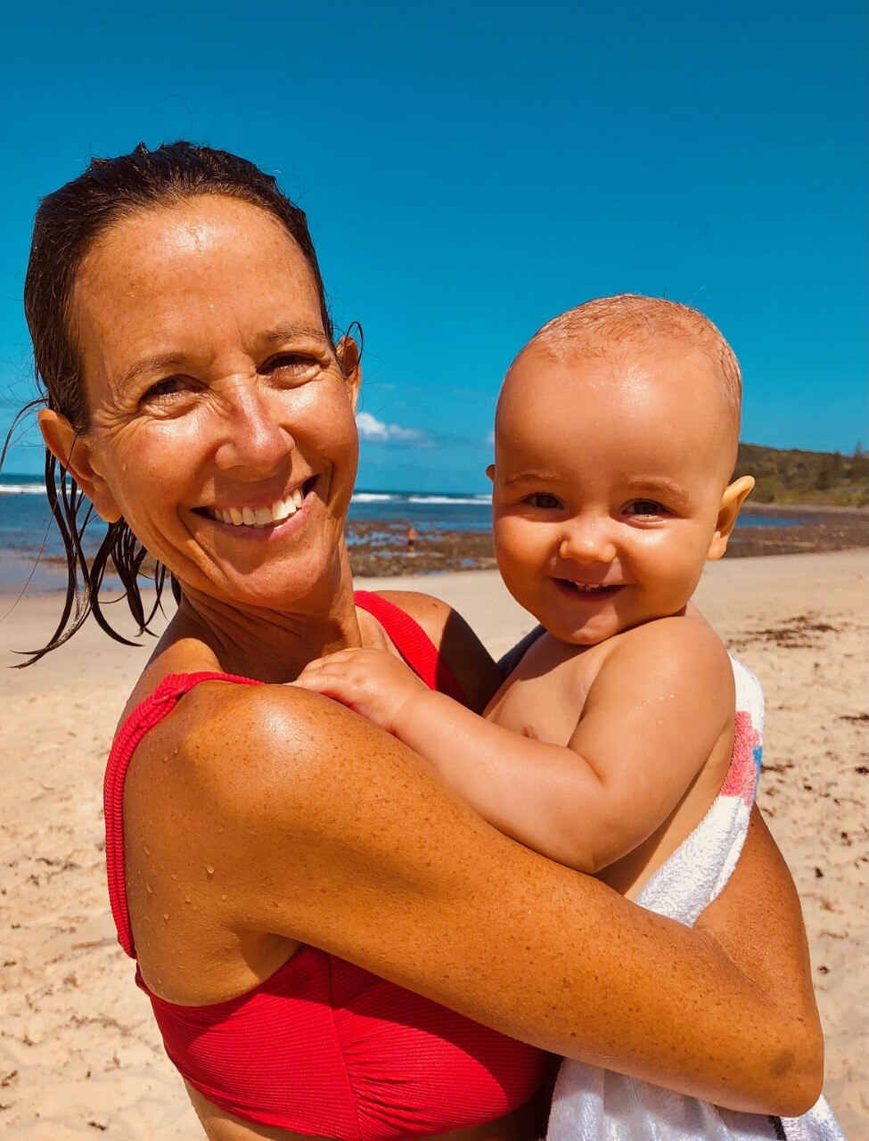 Woman grins on beach holding infant son