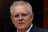 Scott Morrison looks into the distance with an Australian flag behind him