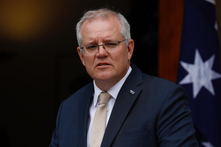 Scott Morrison looks into the distance with an Australian flag behind him
