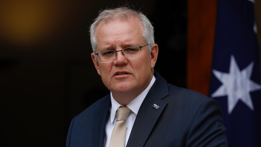 Scott Morrison looks into the distance with an Australian flag behind him