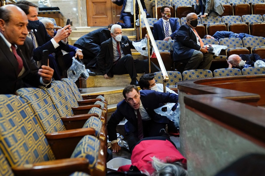 Men in suits crouching in the US chamber looking frightened